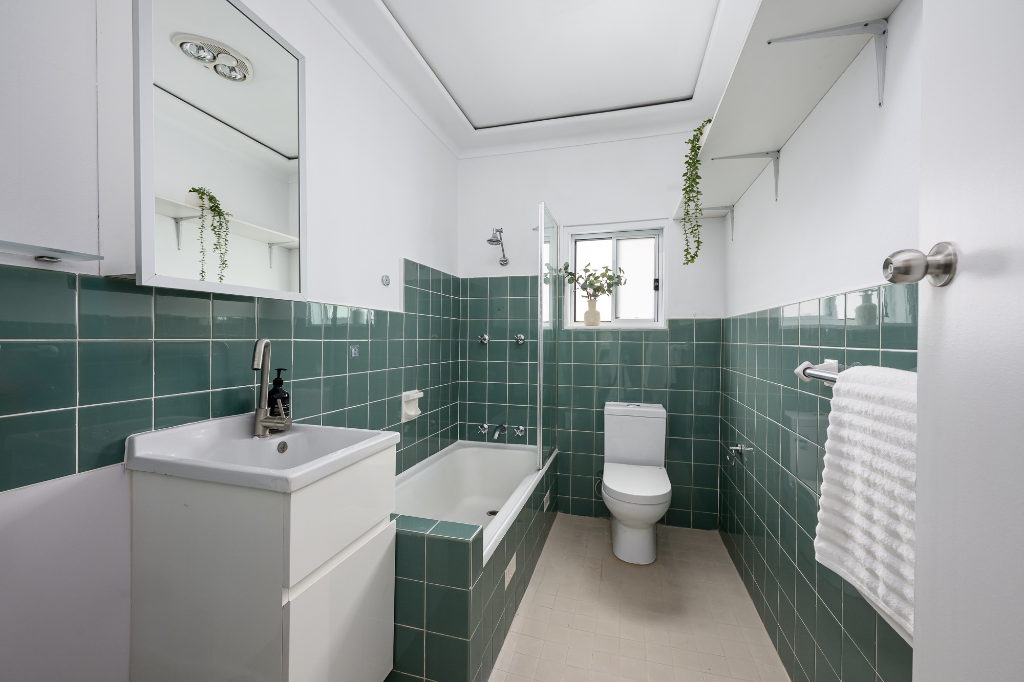 Bathroom with green tiles, white vanity and bath with shower screen